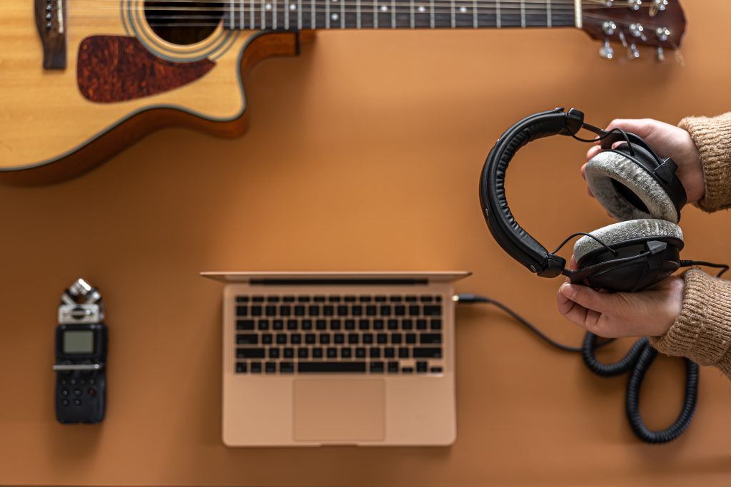 Imagem de mesa com laptop, headphones e violão. Pausa na rotina por meio de outras atividades. Imagem: Reprodução/FreePik.